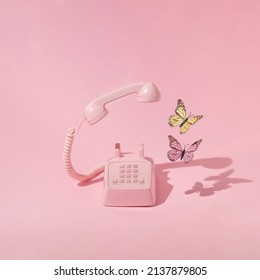Spring creative layout with pink retro phone with colorful butterflies on pastel pink background and green grass. 80s or 90s retro fashion aesthetic telephone concept. Minimal romantic handset idea.