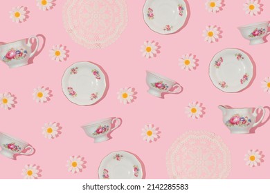 Spring creative pattern vintage tea cups, saucers, embroidery lace placemat and flower heads on pastel pink background. 80s, 90s retro romantic aesthetic summer concept. Fashion tea party idea.