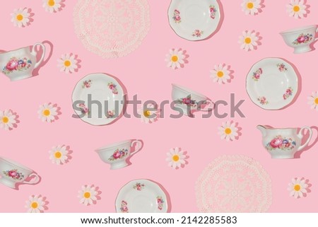 Spring creative pattern vintage tea cups, saucers, embroidery lace placemat and flower heads on pastel pink background. 80s, 90s retro romantic aesthetic summer concept. Fashion tea party idea.