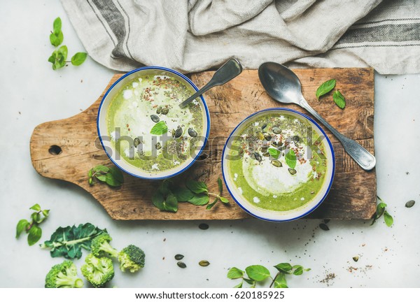 Spring detox broccoli green cream soup with mint\
and coconut cream in bowls on rustic wooden board over marble\
background, top view. Clean eating, dieting, vegan, vegetarian,\
healthy food concept
