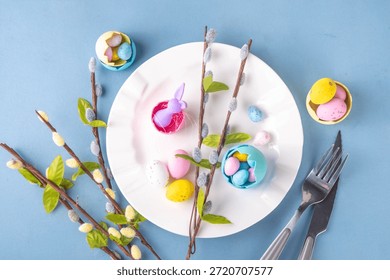 Spring Easter holiday menu table setting, cutlery and plate on pastel blue background with checkered napkin, festive ribbon, Easter festive decor with cute rabbits, Easter chocolate eggs