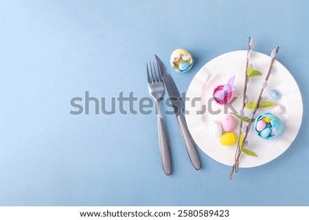 Spring Easter holiday menu table setting, cutlery and plate on pastel blue background with checkered napkin, festive ribbon, Easter festive decor with cute rabbits, Easter chocolate eggs