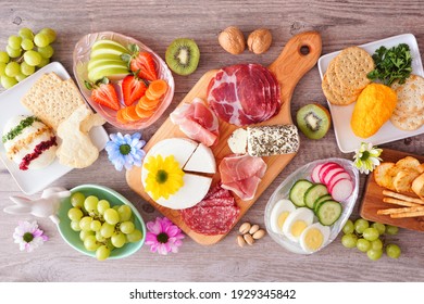 Spring or Easter theme charcuterie table scene against a wood background. Variety of cheese, meat, fruit and vegetable appetizers. Top view.