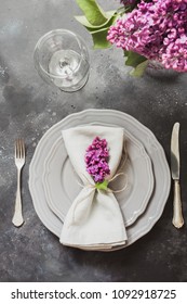 Spring elegant table place setting with violet lilac flowers, silverware on vintage table. Top view.