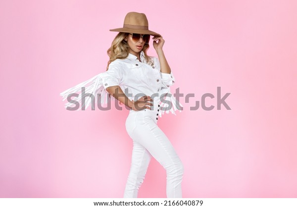 Spring\
fashion. Beautiful stylish female model in white trendy outfit in\
studio. Elegant woman in white fringe jacket and white boots on\
pink background. Studio shoot. Fashionable\
woman.