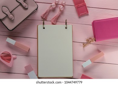 spring flat lay in rose tone. empty notebook and lipstick, rose glasses, earrings, handbag on a pink wooden plank background. flat lay with fashion accessories in pastel  tones