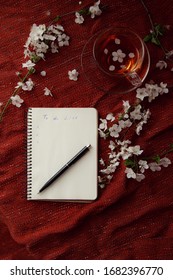 Spring flat lay top view home office workspace - notebook with tea cup and cherry blossom branches on a red desk background