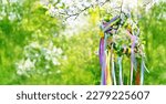 Spring floral wreath with colorful ribbons on tree in garden, green natural background. floral decor. Symbol of Beltane, Wiccan Celtic Holiday beginning of summer. witchcraft, magic ritual. banner