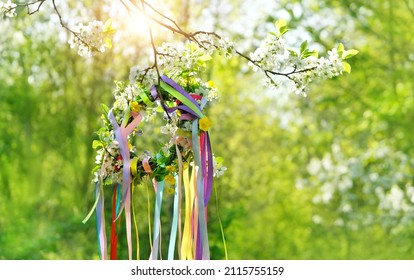 Spring flower wreath with colorful ribbons in garden, green natural background. floral decor. Symbol of Beltane, Wiccan Celtic Holiday beginning of summer. pagan witch traditions and rituals