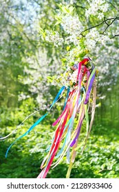 Spring flower wreath with colorful ribbons on cherry tree in garden. floral traditional decor. Symbol of Beltane, Wiccan Celtic Holiday beginning of summer. pagan traditions, magic witch rituals