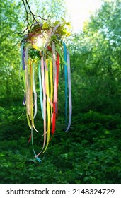 Spring flower wreath with colorful ribbons on tree in forest, green natural background. floral decor, Symbol of Beltane, Wiccan Celtic Holiday beginning of summer season. pagan witch traditions.