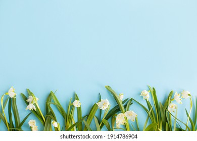 Spring Flowers Border On Blue Paper Flat Lay. Stylish Floral Greeting Card With Space For Text. Hello Spring.  Earth Day Concept. White Spring Snowflakes Flowers Growing On Blue Background