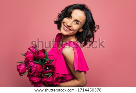 Spring flowers. Young gorgeous girl in a bright pink dress is looking in the camera with a big smile, holding a bunch of tulips in her hands.