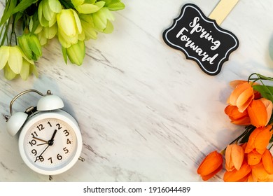 Spring Forward Daylight Saving Time Concept With Text On Marble Flat Lay.  White Alarm Clock With Tulips.