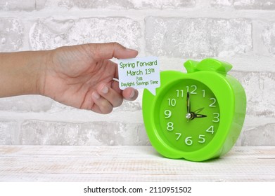 Spring Forward March 2022 Daylight Savings Time comment box held in held next to clock on whitewashed wood  - Shutterstock ID 2110951502