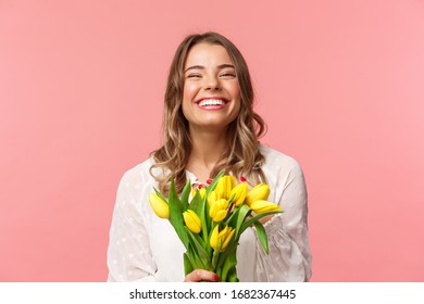 Spring, happiness and celebration concept. Close-up of happy and carefree blond european girl receive beautiful bouquet of flowers, holding yellow tulips, smiling and laughing, pink background - Powered by Shutterstock