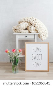 Spring Home Interior Decor: White Knitted Woolen Merino Chunky Plaid, Bedside Table, Frame With Text HOME SWEET HOME, Glass Vase, Tulips Flowers. Blanket Of Thick Yarn. Cozy Scandinavian Room Interior