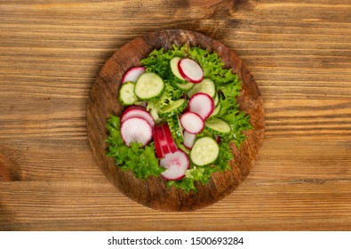 Spring Homemade Radish Salad With Fresh Cucumber And Greens On Wooden Plate Top View. Simple Green Rustic Salat With Sliced Radishes, Cucumbers, Escarole And Lettuce