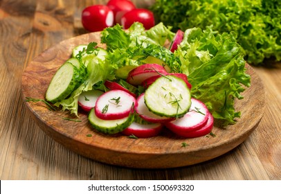 Spring Homemade Radish Salad With Fresh Cucumber And Greens On Wooden Plate Front View. Simple Green Rustic Salat With Sliced Radishes, Cucumbers, Escarole And Lettuce