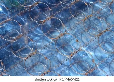 Spring Mattress Wrapped In Plastic Film Wrap Creates A Geometric Texture And A Repetitive Pattern With Its Circular Spring Wires. It Is Thrown Out To The Street As Garbage.