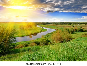 Spring meadow, meandering river, bright sun and blue sky in the evening.