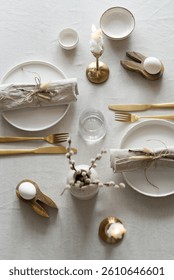 Spring minimalist table setting in warm neutral colors. Easter festive table decoration, white plates, gold cutlery, candles, eggs and willow branches in vase