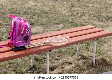 Spring. On the bench is a children's backpack and badminton rackets. Sunny day.