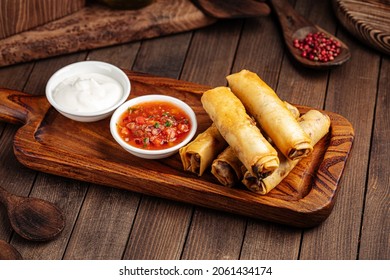 Spring rolls with salsa sauce and sour cream on the wooden background