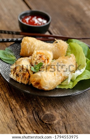 spring rolls and sweet chili sauce on a modern black plate on a wooden table
