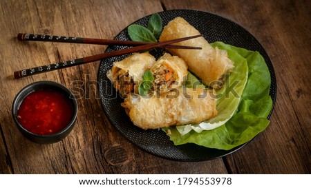 spring rolls and sweet chili sauce on a modern black plate on a wooden table
