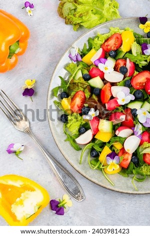 Spring salad of fresh vegetables decorated with edible flowers. Top view.