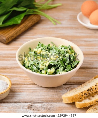 Spring salad of wild garlic and boiled eggs in a ceramic bowl on a wooden background. The use of wild plants for food, the first spring greens. Healthly food