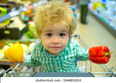 Spring shopping, vegetable purchase. Cute kid with a cool funny face in a store of vegetables and healthy food. A beautiful family, children face looks at the camera. Yellow and red pepper for dinner