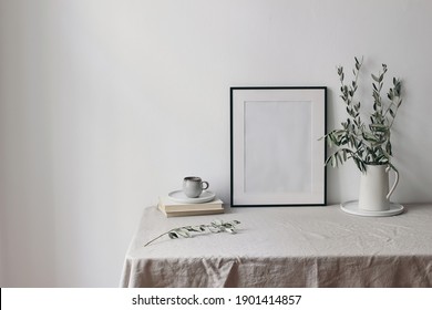 Spring, summer breakfast still life scene. Cup of coffee, books and empty black picture frame mockup. Beige linen tablecloth. Olive tree branches in ceramic jug. Farmhouse, Scandinavian interior.