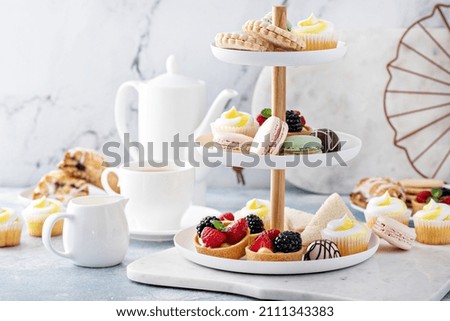 Spring or summer dessert table, three tiered tray with variety of desserts and sandwiches for tea