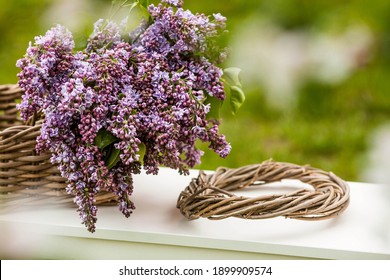 Spring time. A beautiful bouquet of lilacs in a wicker basket of vines on a white bench in the spring garden. Beautiful postcard for printing. The concept of spring and holiday. copy of the text space