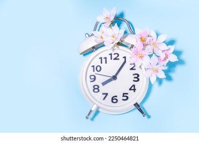 Spring Time Change background. Beautiful fresh spring tree flowers with alarm clock on light blue sunny background top view copy space - Shutterstock ID 2250464821