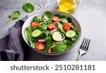 Spring vegan salad with spinach, cherry tomatoes, corn salad, baby spinach, cucumber and red onion. Healthy food concept. Gray stone table. Top view. Copy space