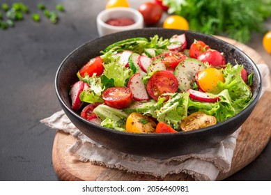 Spring Vegetable Salad With Olive Oil And Sumac In A Black Bowl On A Dark Background. Salad Of Radishes, Cucumbers, Tomatoes, Lettuce, Sumac, And Olive Oil. Vegan Or Diet Food. Healthy Lunch.