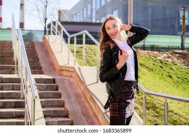 Spring vertical photo of a happy smiling beautiful girl with emotions in the sun outdoors on the background of the steps in the city. Pretty model posing in front of the camera. - Shutterstock ID 1683365899