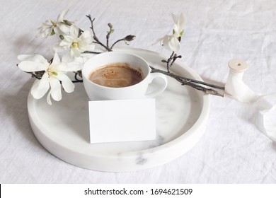 Spring wedding still life scene. Business, place card mockup, marble tray, cup of coffee. Vintage feminine styled photo. Floral composition with star magnolia blooming branches on white linen table.
