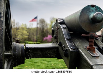 Springfield, MO—April 11, 2019; Bronze Civil War Era Confederate Cannon Points Toward American Flag At Wilsons Creek National Battlefield In Southwest Missouri In Spring