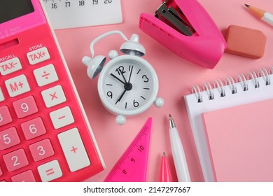 Spring-loaded notepad, white pencil, pink and white pen, rulers, pink stapler, alarm clock on a pink background.Things for businessmen, schoolchildren, students, teachers, artists, education