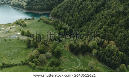 Springtime aerial view of open fields, scattered cottages, and deep forest beside Zaovine Lake in Serbia. Tara National Park