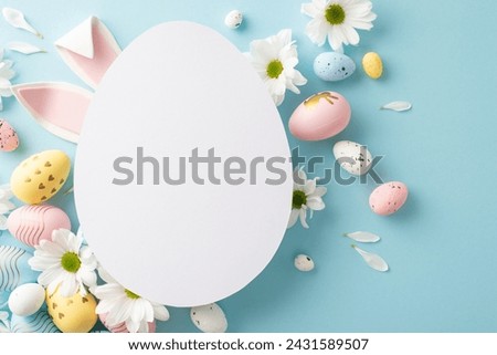 Springtime charm captured in top view photo: pastel-colored eggs, bunny ears, fresh daisies on a soft blue backdrop, complemented by a cut-out card in the shape of an egg for heartfelt Easter messages