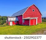 A springtime image taken on the trail leading to the open doors of a big red barn on a sunny day.