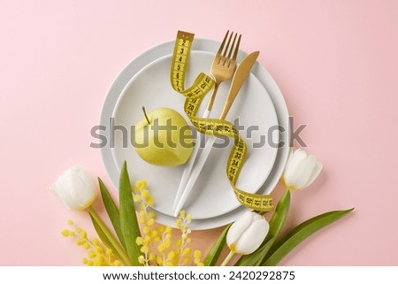 The springtime slimdown: nutritional strategies for a lighter season. Top view shot of plates, cutlery, apple, measure tape, flowers on pink background