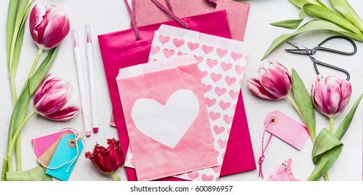 Springtime Workspace With Tulip Flowers , Shears, Pink Paper Bags And Envelope With Heart, Top View, Copy Space. Gift And Greeting Card Making For Mothers Day