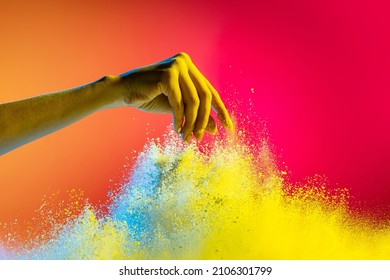 Sprinkle mystical sand. Female hand and explosion of colored, neoned powder on pink studio background in neon light. Trendy colors - pink, white and yellow. Festival, design, beauty concept.