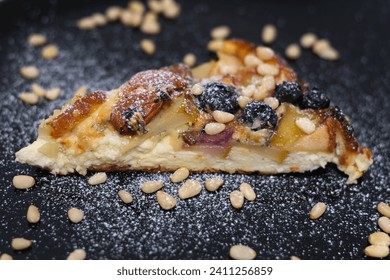 sprinkle with powdered sugar delicious pie with pear and Brit cheese curd cheesecake nuts almonds and cashews on black snow-covered plate with sugar delicious appetizing dessert serving blueberries - Powered by Shutterstock